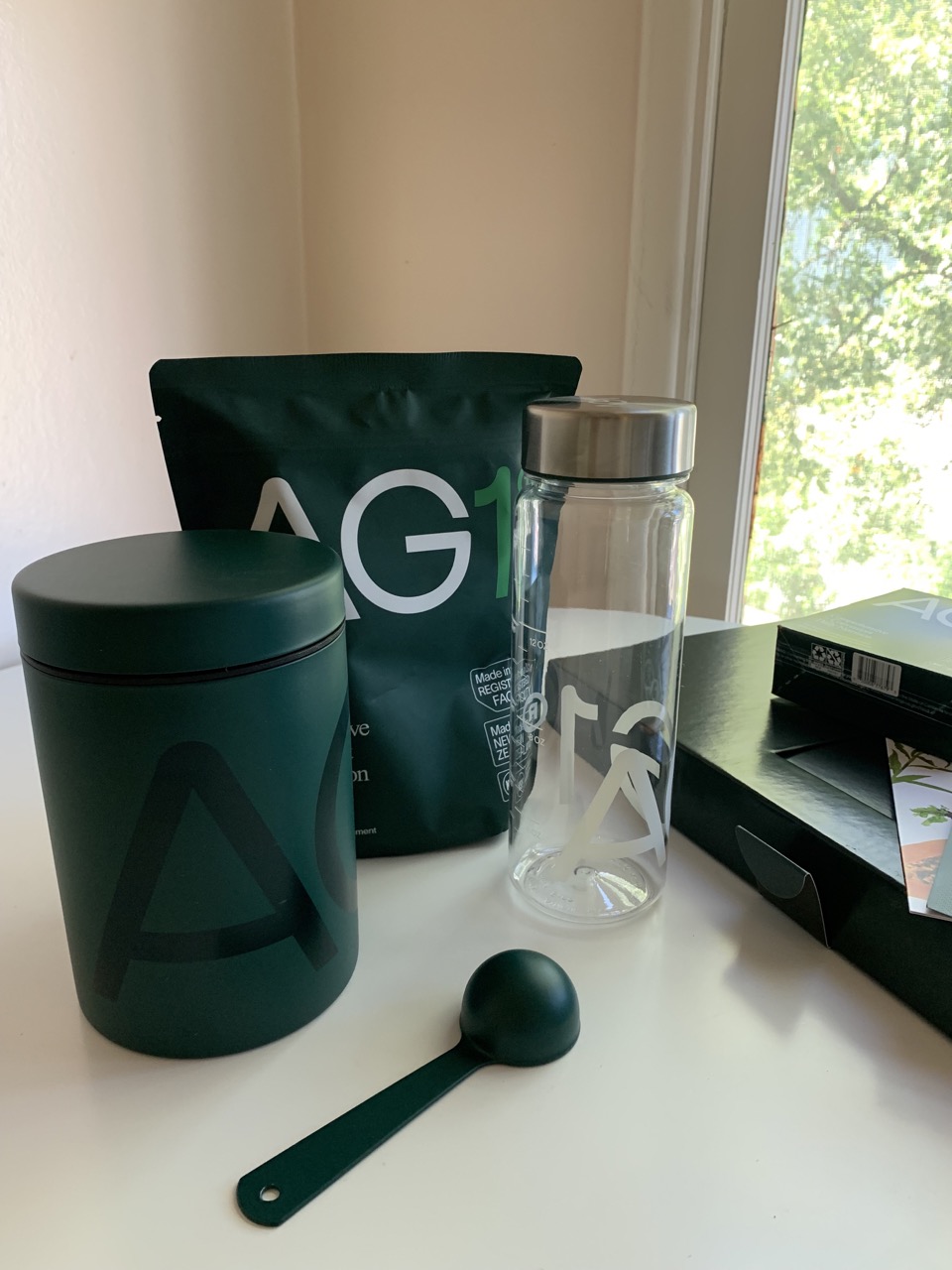 An image of the bag of AG1, the canister, metal scoop, and bottle that comes with the first purchase