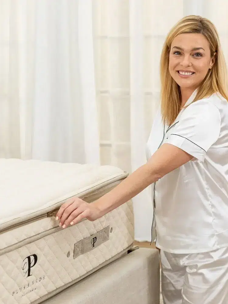 A model stands next to a Plushbeds mattress