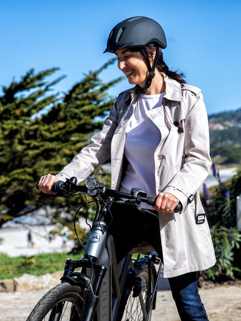 A model in a white trench coat holding onto the handlebars of a Gazelle e-bike. 