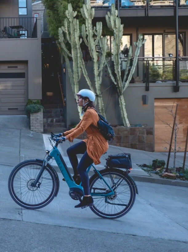 A model riding up a hill on a blue Gazelle e-bike. 