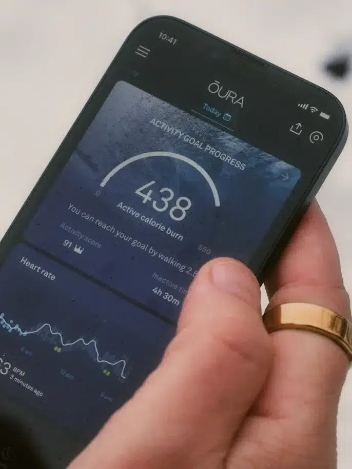A model's hand holding a smartphone showing the app for Oura Ring