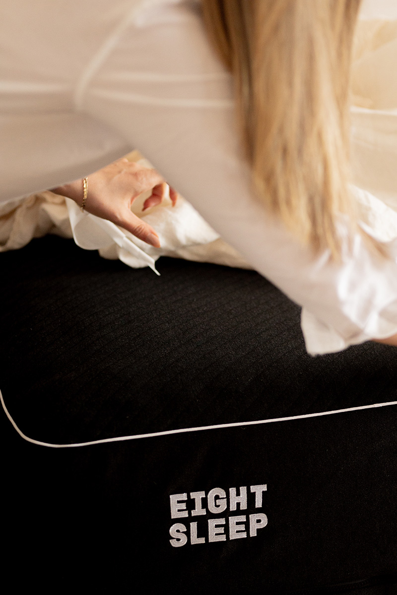 Woman in a white blouse adjusting a black "eight sleep" branded mattress cover.