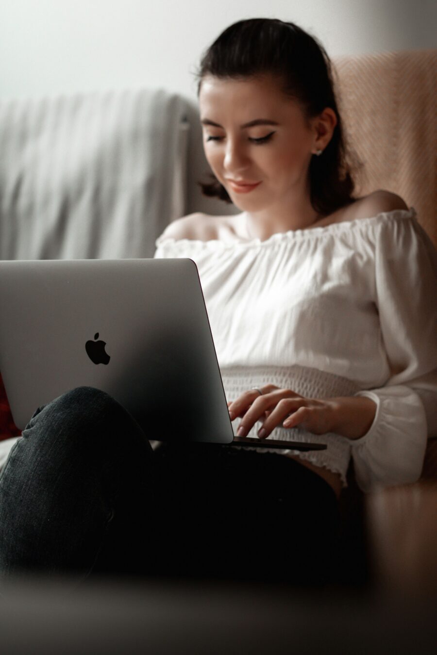 A young woman in a white shirt uses a laptop that sits in her lap.