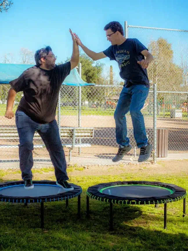 Two men high five while jumping on rebounder trampolines from Leaps and Rebounds
