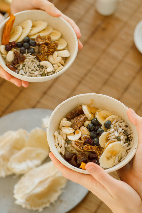 Two pairs of hands hold bowls full of fruit and paleo oatmeal