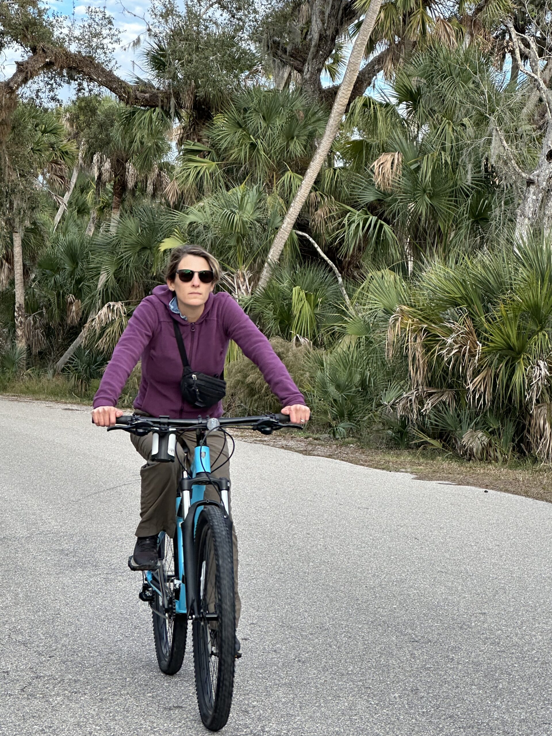 A woman riding a bike down a road with palm trees.