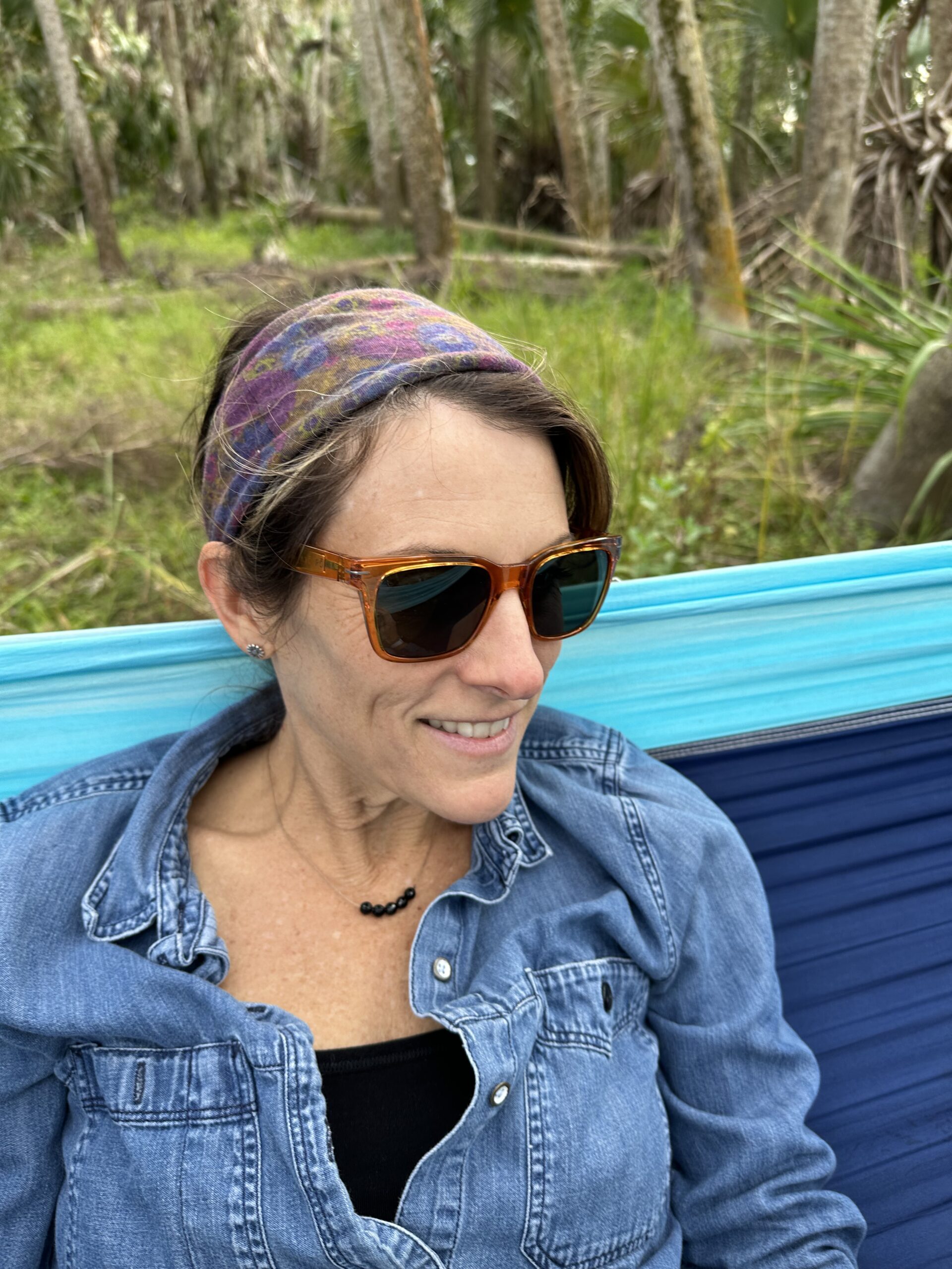 A woman wearing sunglasses and a headband in a hammock.