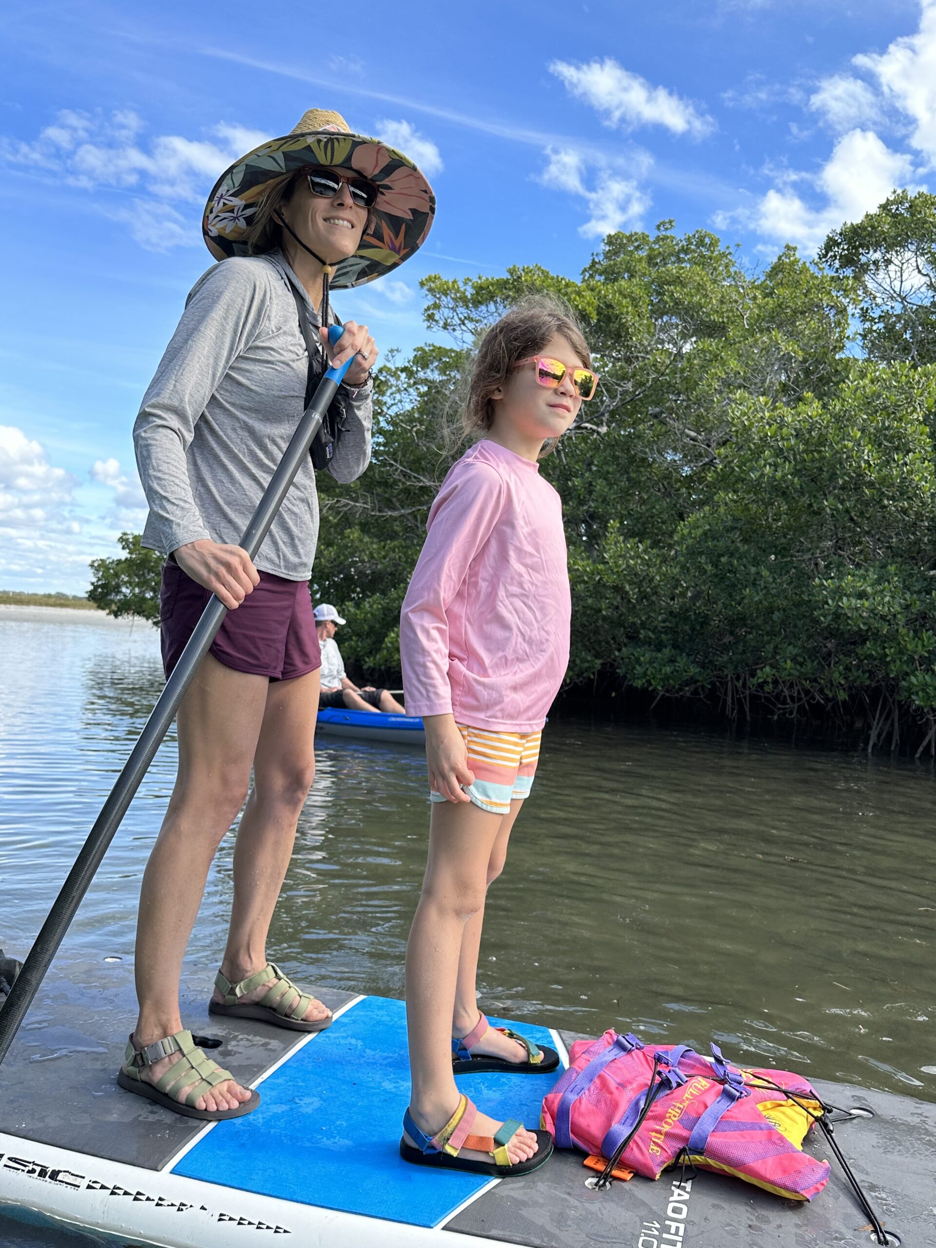 A woman and a girl stand on a paddle board in the water.