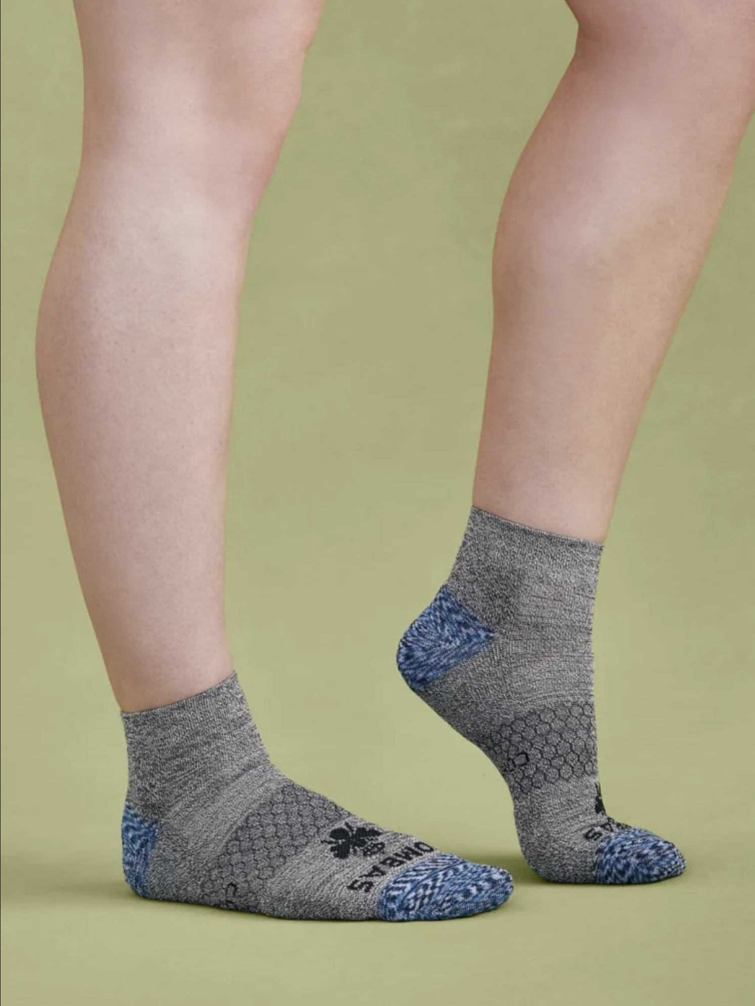Person wearing gray compression socks with blue toes on a green background.