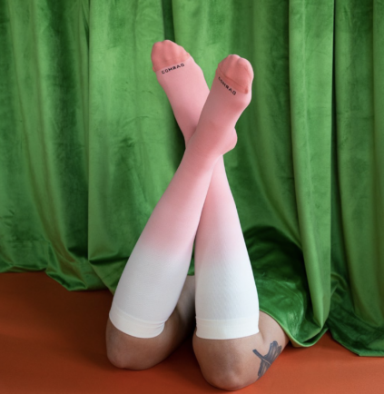 A pair of legs crossed over, wearing pink and white knee-high compression socks.