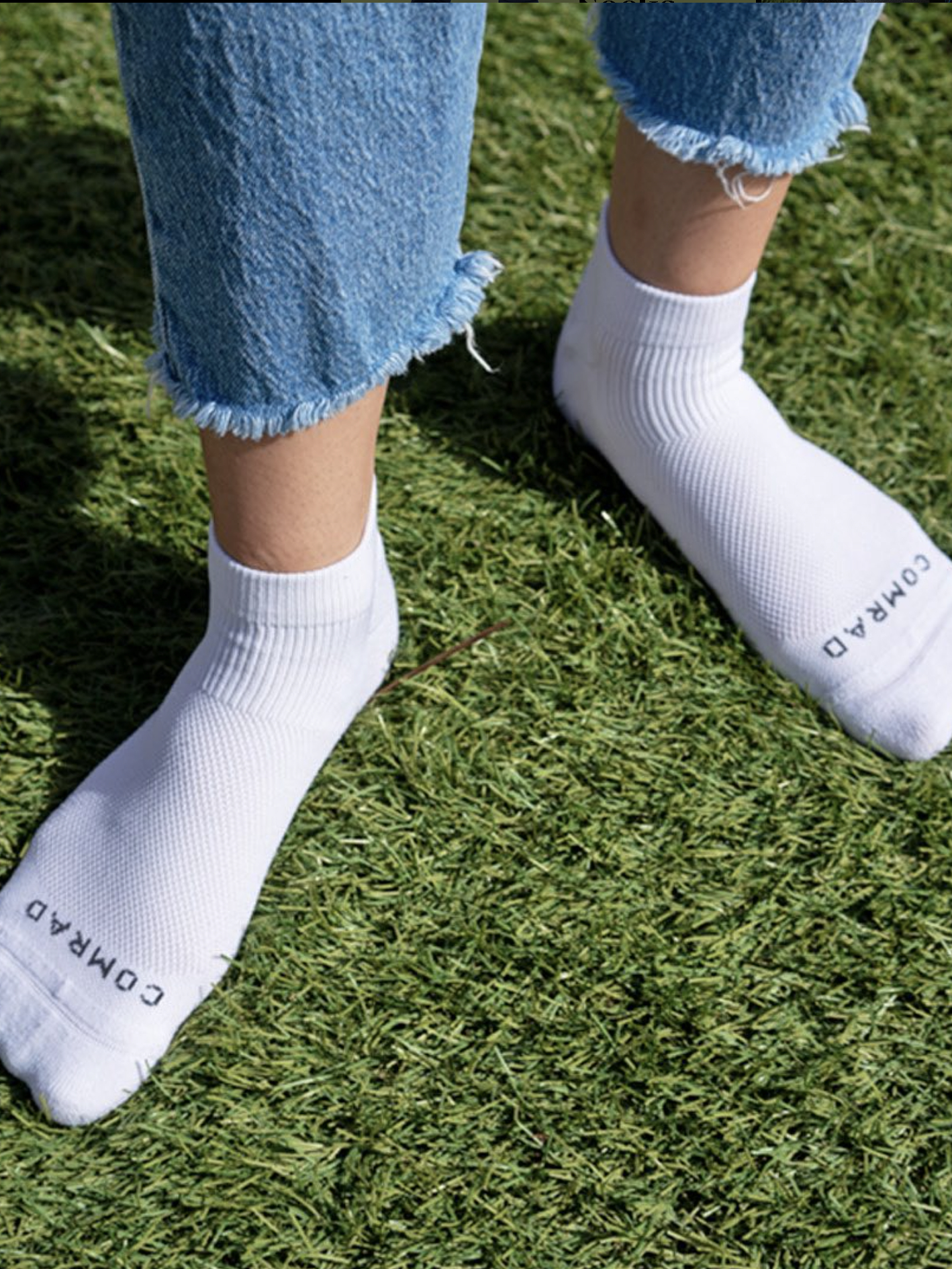 A person standing on grass wearing white compression socks and blue jeans with frayed hems.