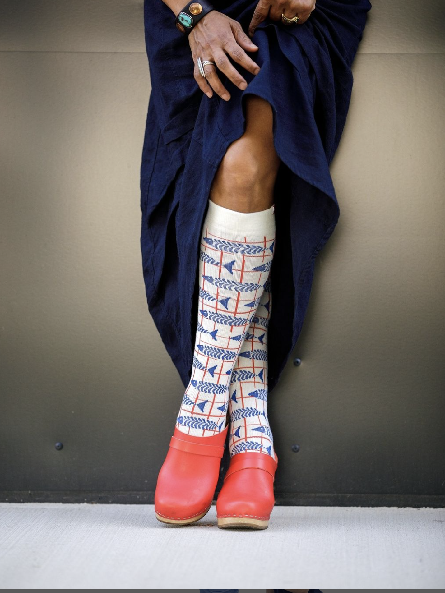 A person wearing patterned compression socks and red rubber boots, with a dark blue garment draped over.