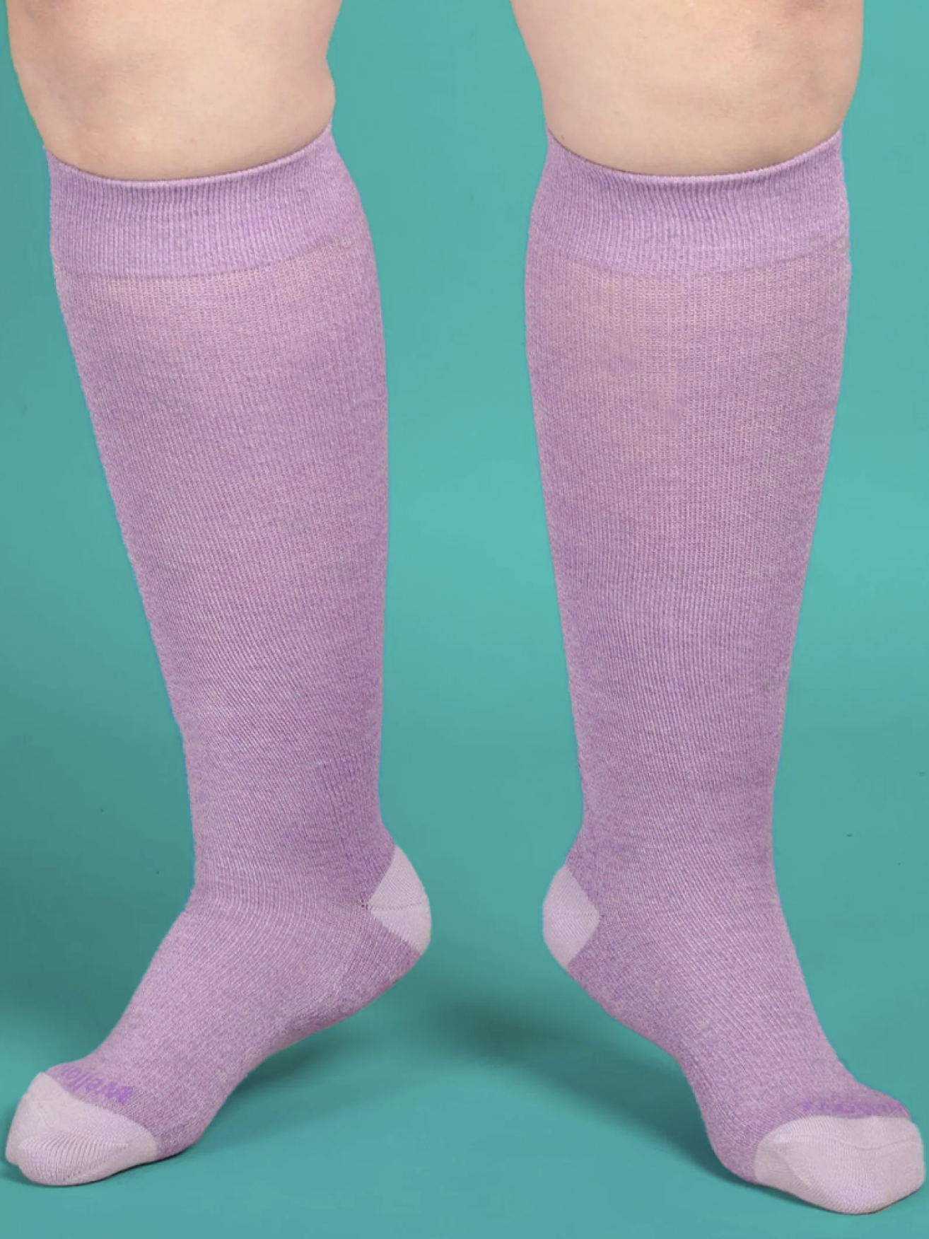 A person standing against a teal background, wearing purple knee-high compression socks.