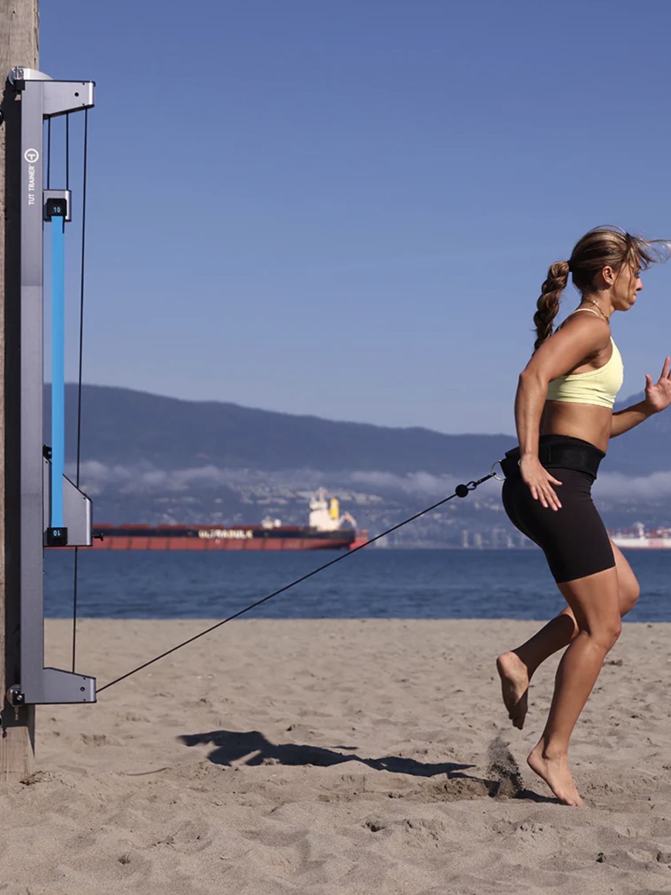 A woman exercising with a home gym on a beach.