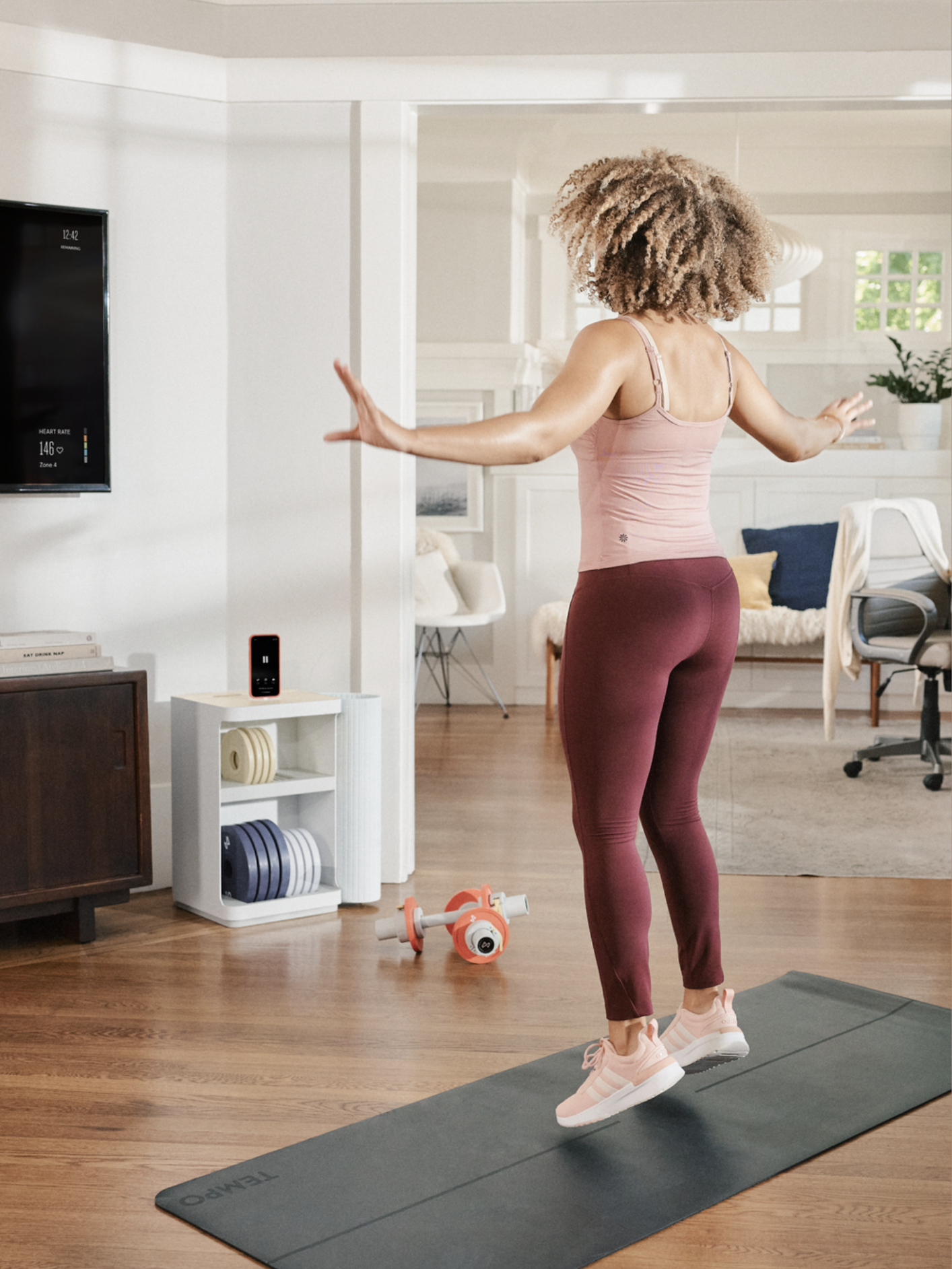 A woman exercising at home while following a workout routine on a television screen.