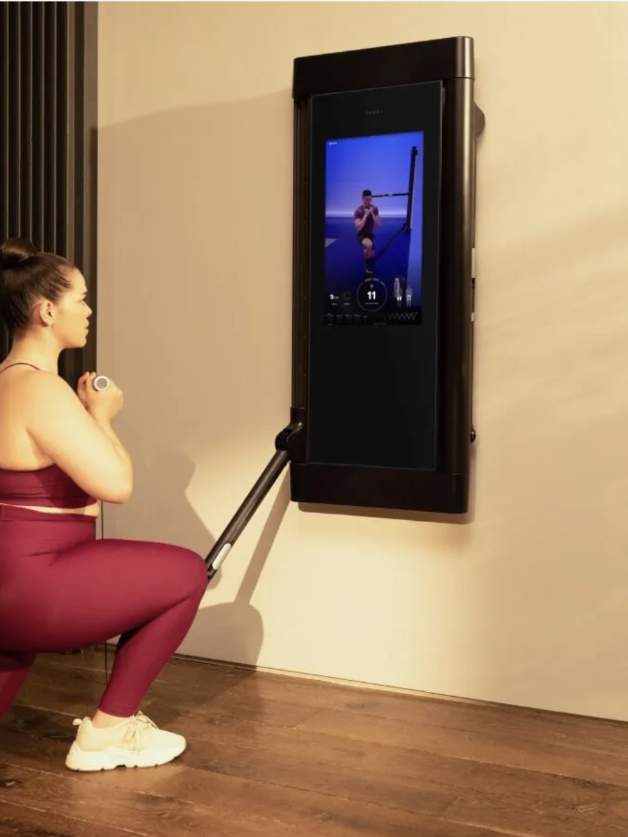 Woman exercises at home using a wall-mounted digital fitness system.