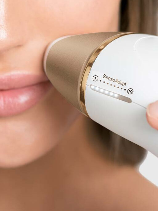 A woman uses a laser hair removal device from Braun.