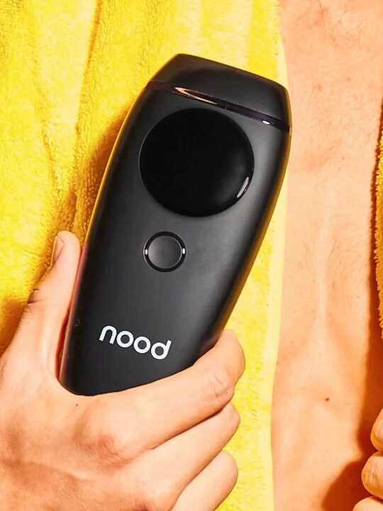A man in a yellow towel holding black laser hair removal device from nood.
