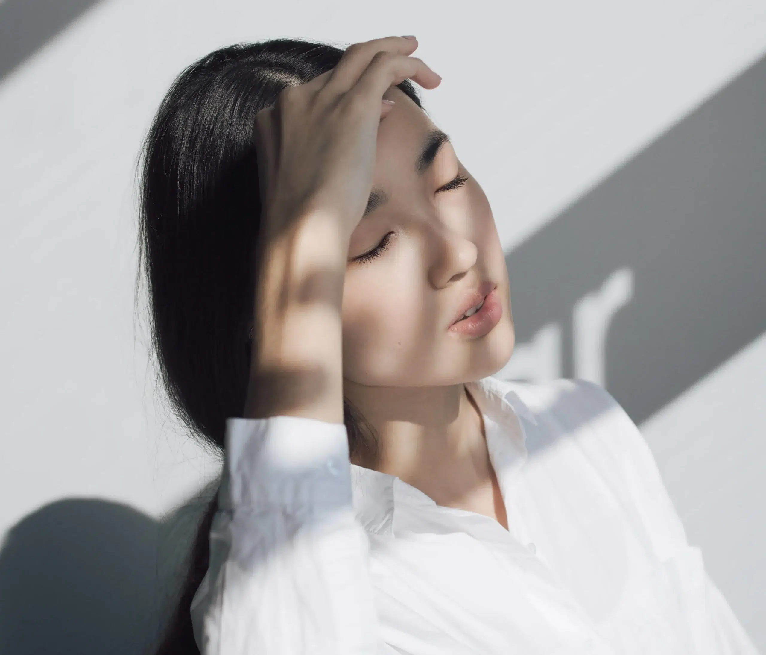 A young Asian woman with massage guns in her hands, resting on her head.