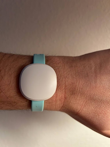 A wrist wearing a turquoise band with a white circular face, possibly a smartwatch or fitness tracker.