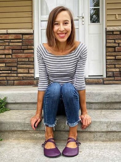 A woman sitting on a set of steps outside wearing Mary Janes, jeans, and a striped shirt.