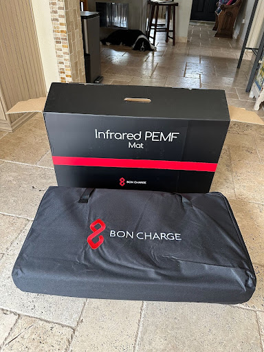 An infrared pemf mat by bon charge unpacked and displayed next to its box in a home environment.