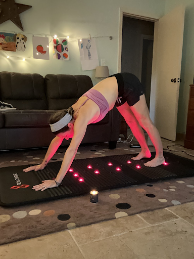 A person performing a downward-facing dog yoga pose on a mat with red light therapy.