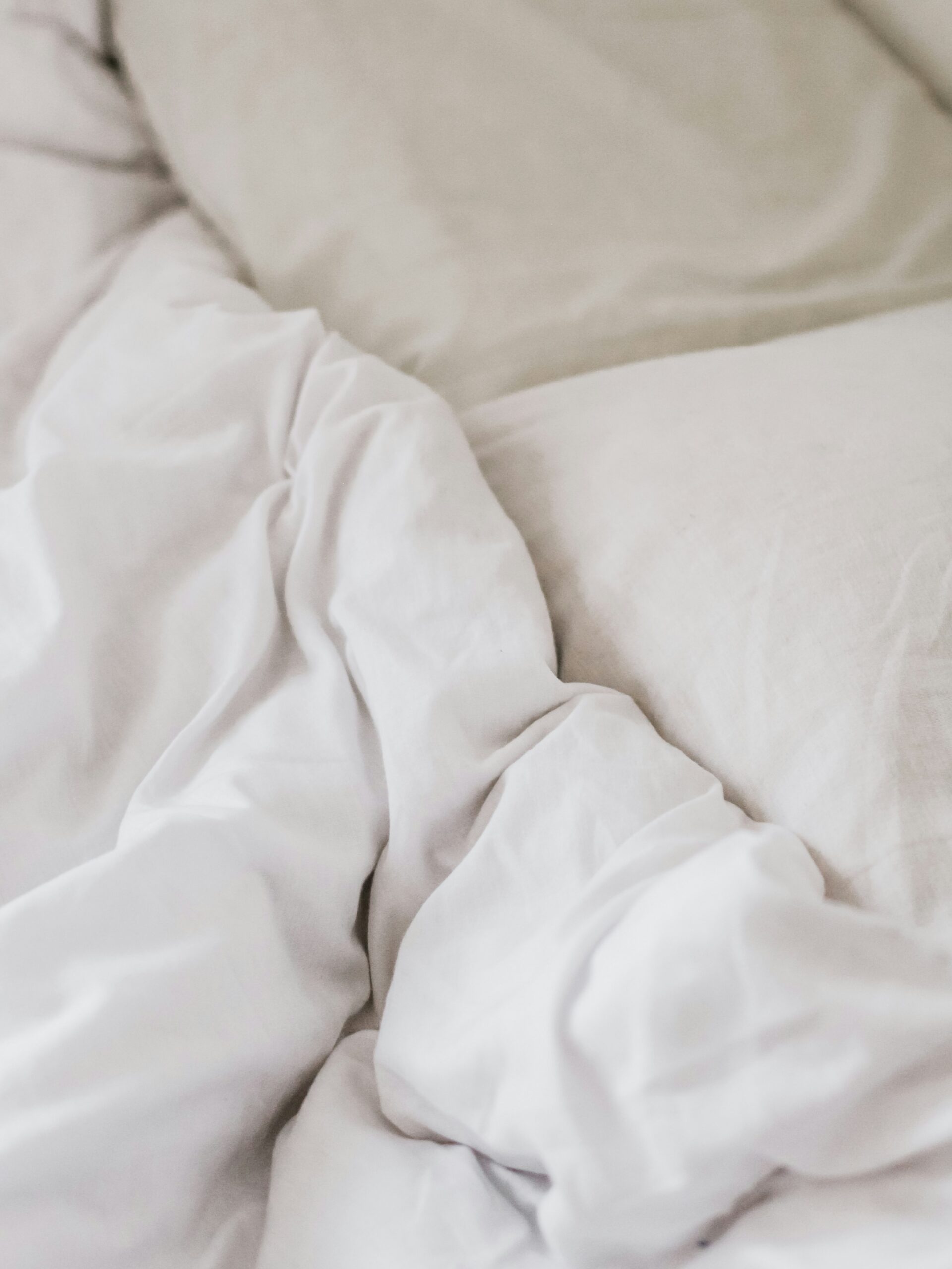 A close-up of white, wrinkled bed sheets and pillows on a bed.