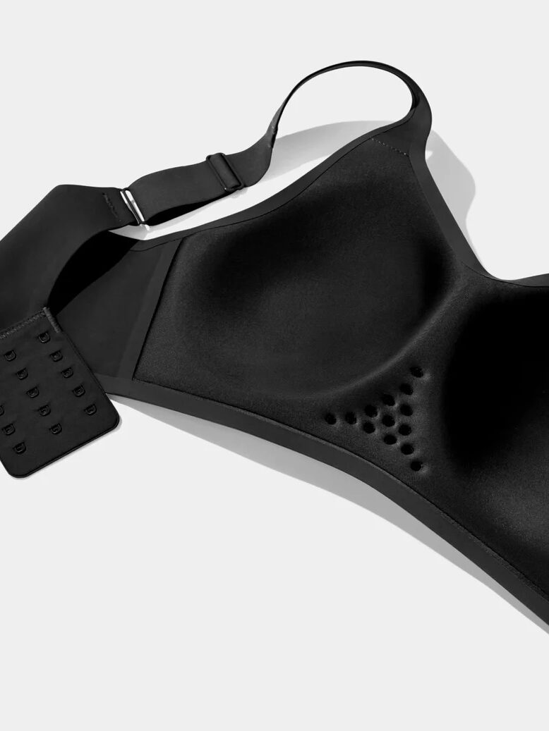 Black sports bra with molded cups, multiple hook-and-eye closures, and perforated detailing, reminiscent of the precision engineering seen in massage guns, laid flat on a white background.