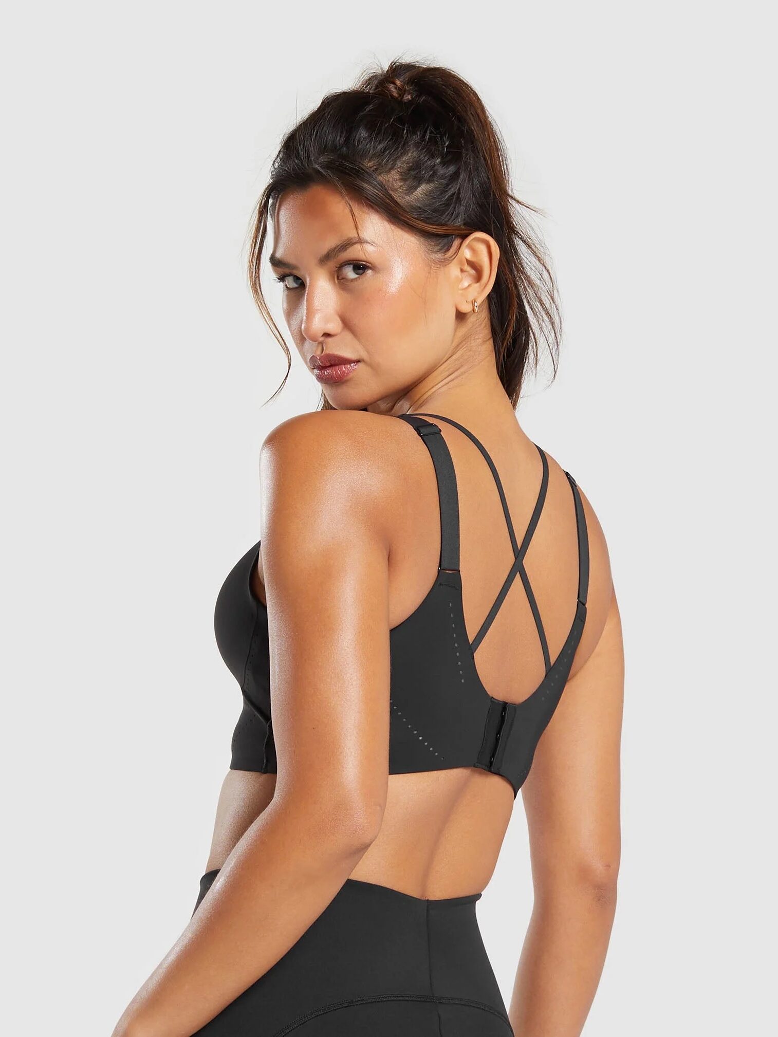 A person in a black sports bra with crisscross straps at the back, looking over their shoulder against a plain background, as if paused right before using one of those sleek massage guns.
