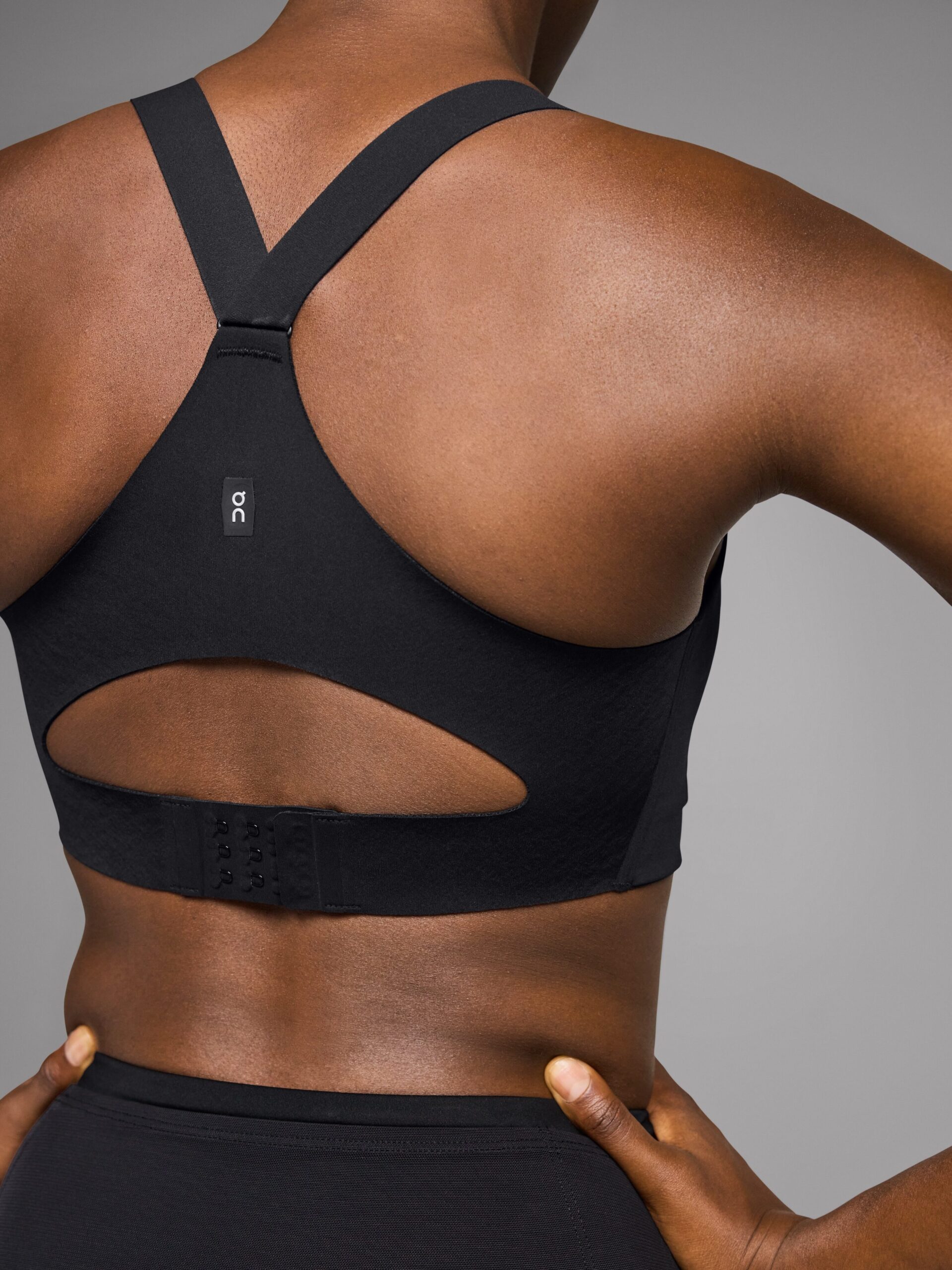 Back view of a person wearing a black sports bra and high-waisted leggings. The bra features a racerback design with a cutout and adjustable hook closures, perfect for pairing with massage guns to soothe post-workout muscles.