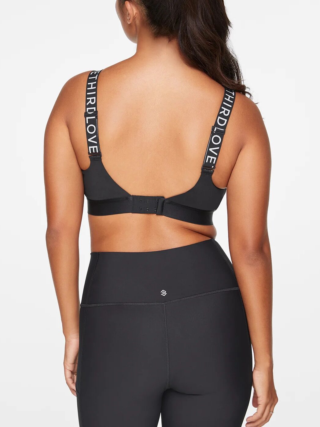 A woman in a black sports bra and leggings showcases her toned back. The straps, emblazoned with "THIRD LOVE," hint at hours of dedicated workouts, perfectly complemented by soothing sessions with massage guns.