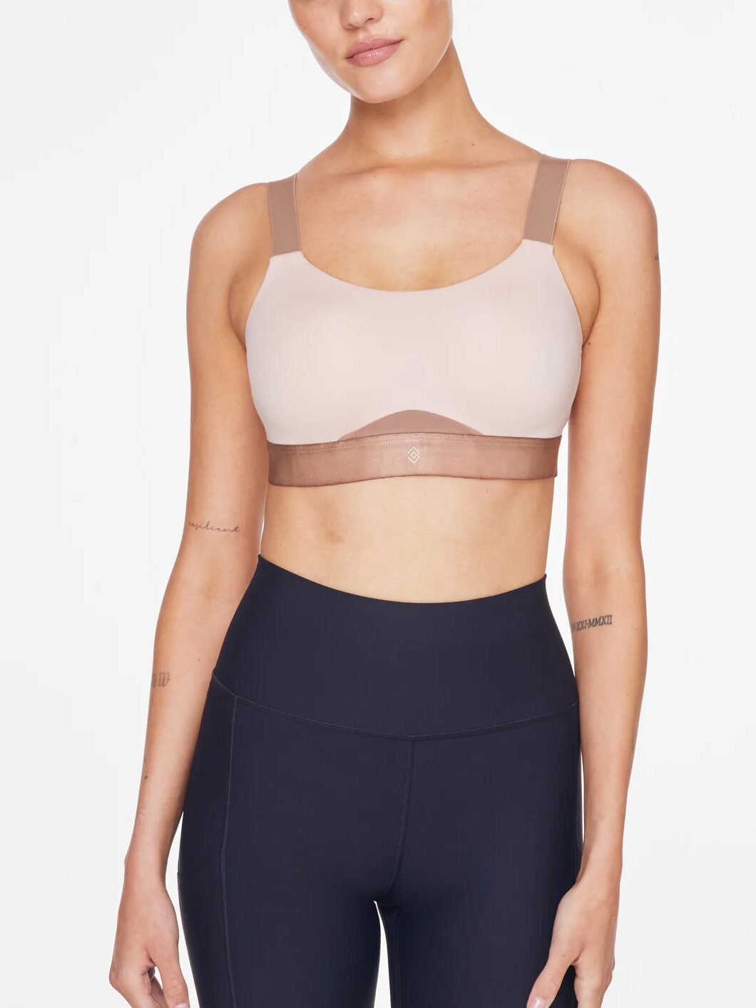 A person in a beige sports bra and black leggings poses against a plain background, perhaps unwinding post-workout with massage guns to ease muscle tension.