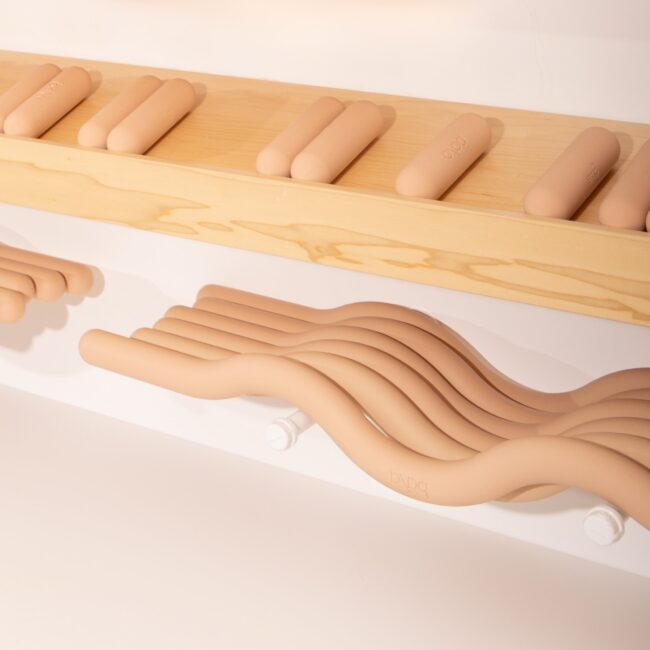 Several smooth, tan-colored cylindrical and wavy objects are displayed on wooden and white shelves against a white background.