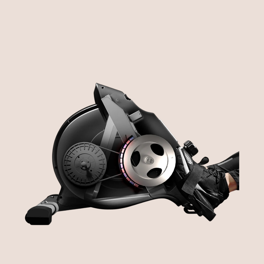 A close-up view of a person's foot secured in the pedal strap of a stationary exercise bike against a plain background, highlighting equipment often paired with massage guns for post-workout recovery.