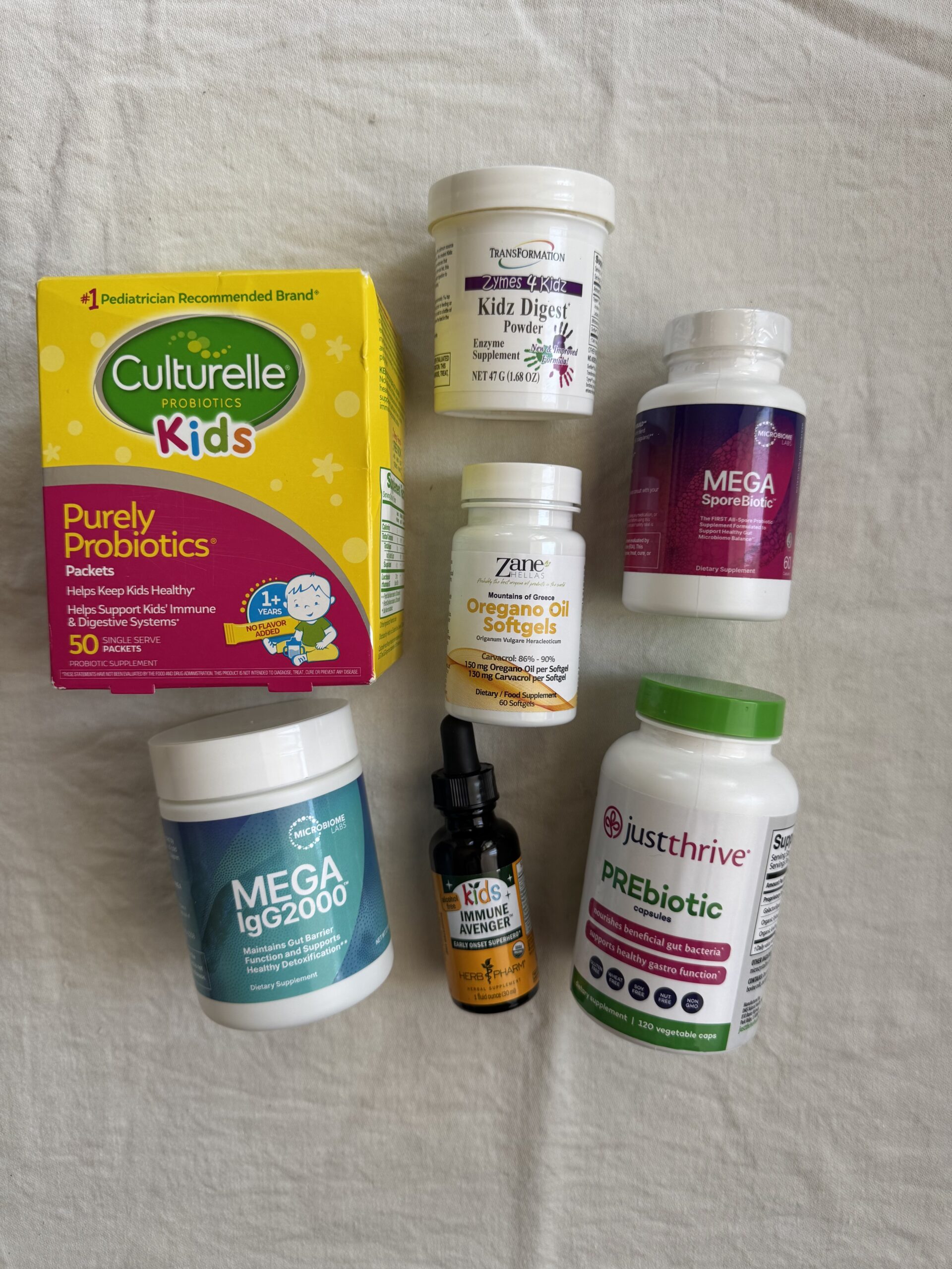 Assorted children's dietary supplements, including probiotics, prebiotics, immune support capsules, and a liquid supplement, arranged on a white surface.