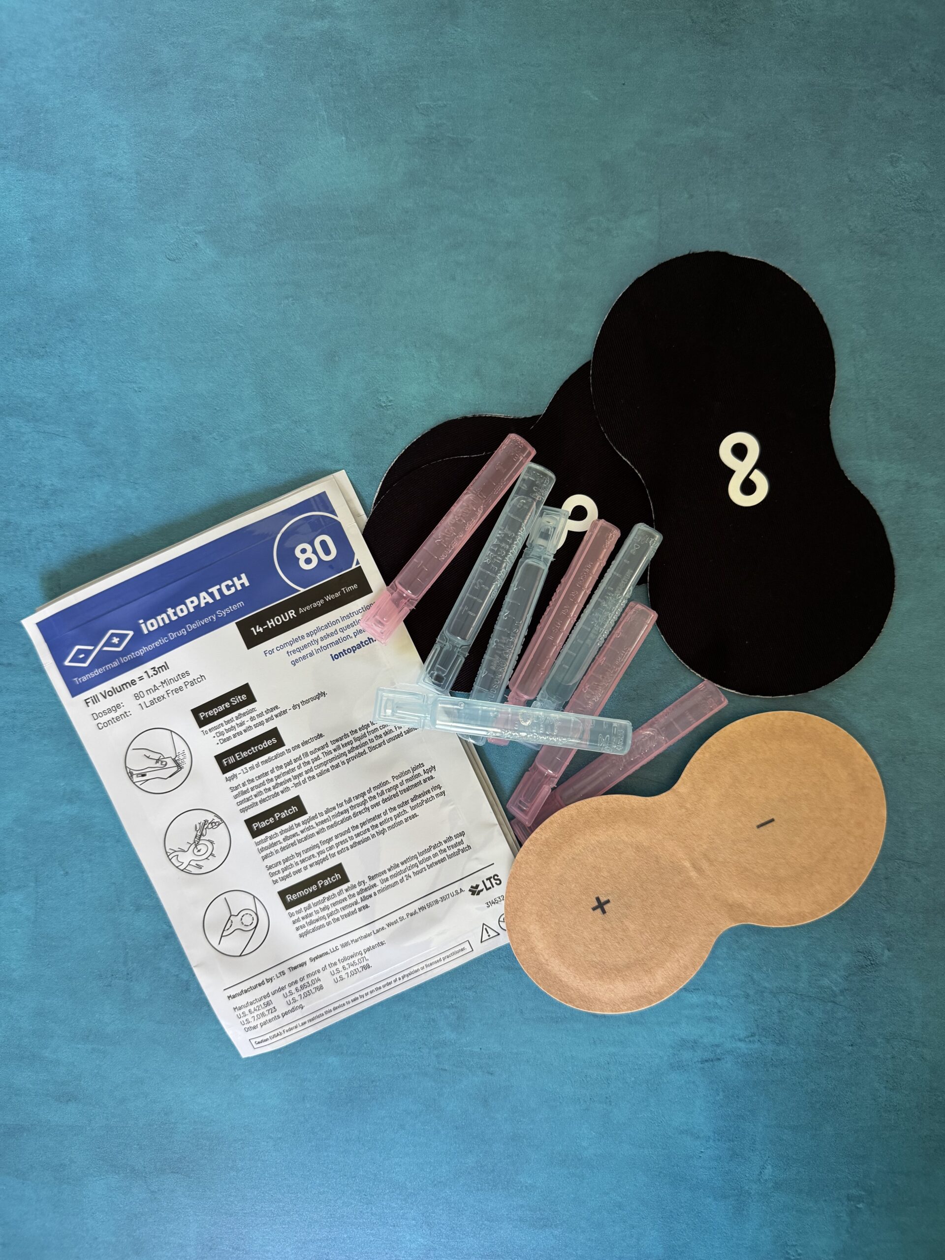 Medical patch kit including instruction sheet, several black and tan patches, and plastic applicators arranged on a blue surface.