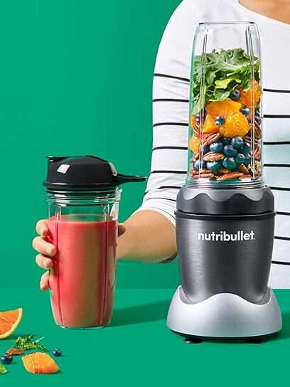 A person stands behind a Nutribullet blender filled with kale, orange slices, and beans; beside them is a massage gun, while they hold a sealed cup of pink smoothie. Ingredients are spread out on the table.