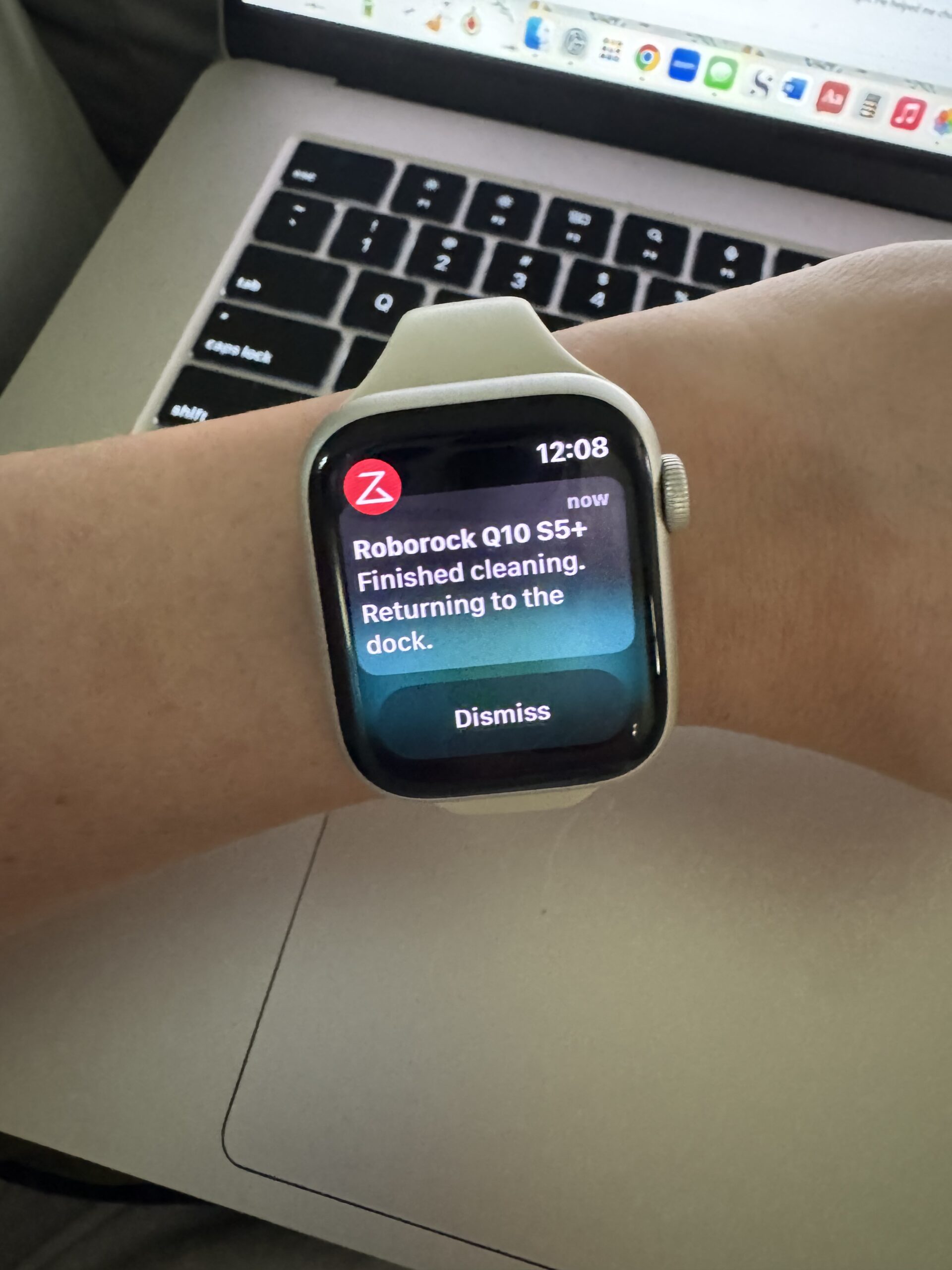 A smartwatch displays a notification stating "Roborock Q10 S5+: Finished cleaning. Returning to the dock" above a laptop keyboard.