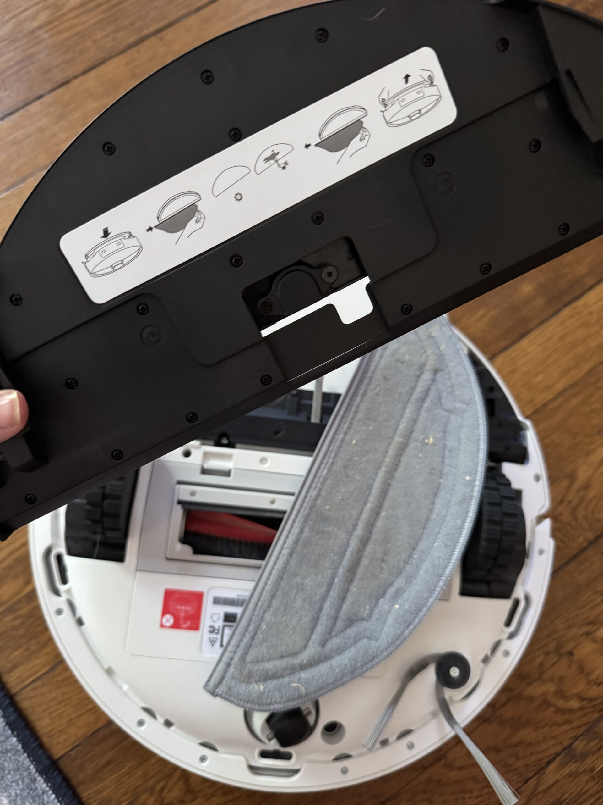 Close-up of a robotic vacuum cleaner with its cleaning pad removed, showing the underside and mop attachment instructions on the detached part.