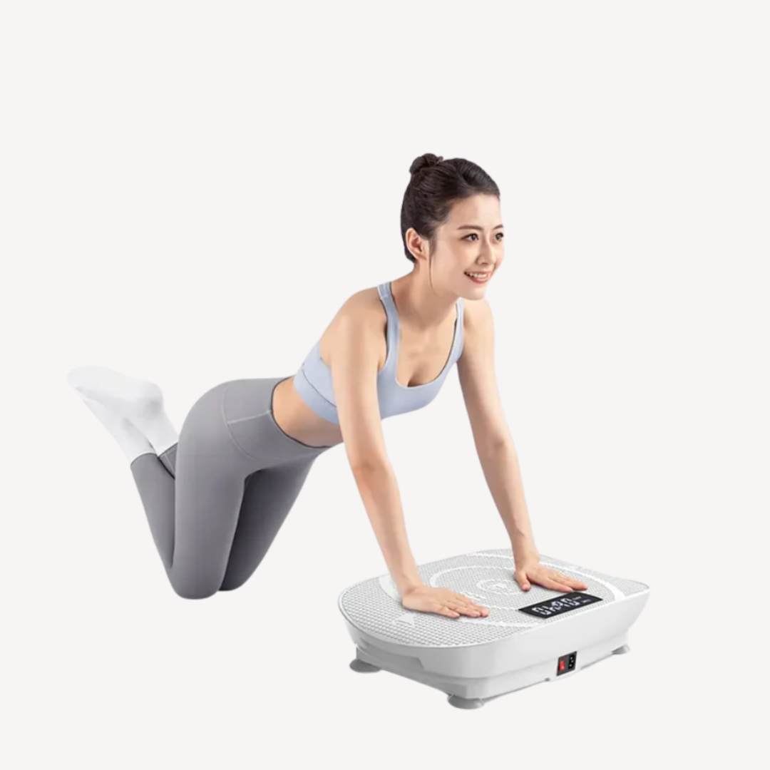 A woman in athletic wear kneels and presses her hands on a white vibration plate exercise machine, with massage guns resting nearby, against a plain background.