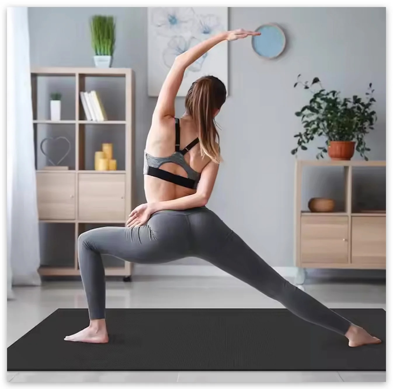 Woman in athletic wear practicing a yoga pose on a mat in a living room with shelves, plants, and wall art—massage guns nearby for post-workout recovery.