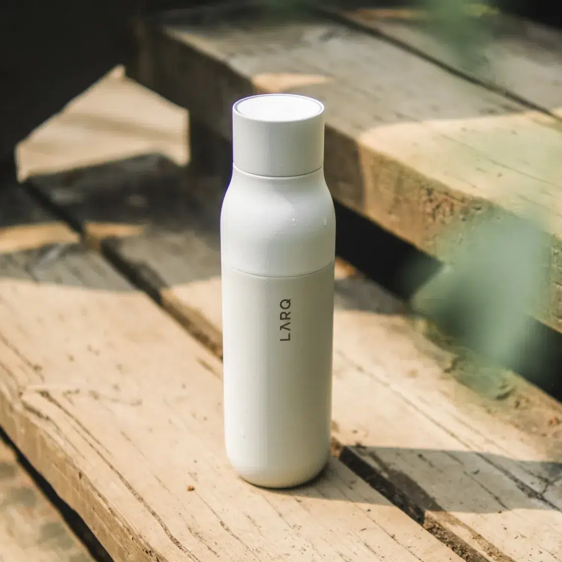 A white LARQ smart waterbottle is placed upright on wooden outdoor steps in natural light.