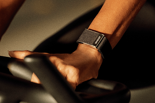 A person’s hand grips exercise equipment while wearing a black WHOOP fitness tracker on their wrist.