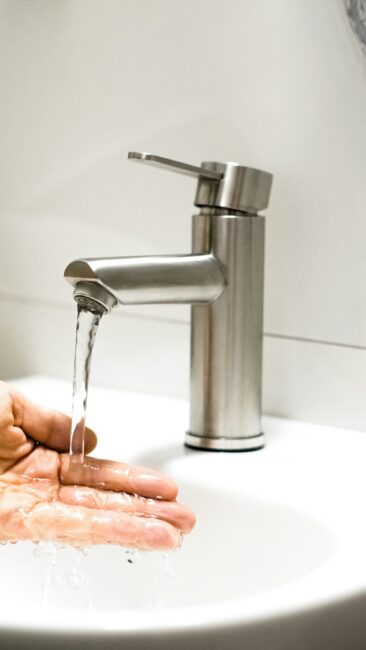 A person holds their hand under running water from a modern stainless steel faucet in a white sink.