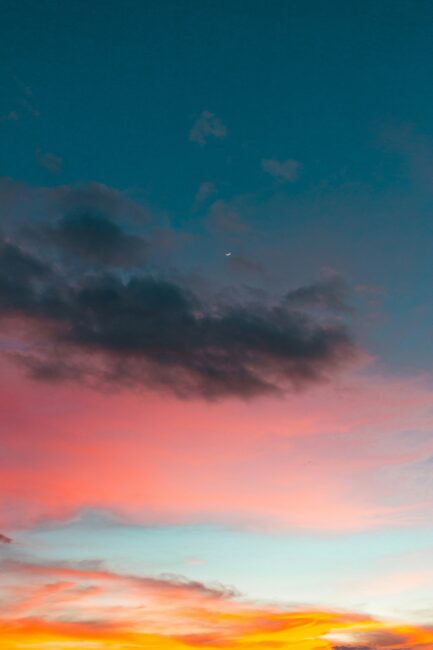 Colorful sky at sunset with blue, pink, and orange clouds; a small crescent moon is visible in the center of the image.