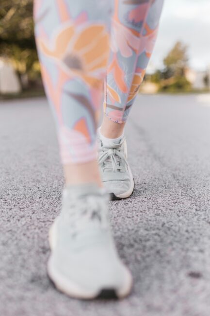 Close-up of a person walking outdoors on pavement, wearing white sneakers and colorful floral-patterned leggings.
