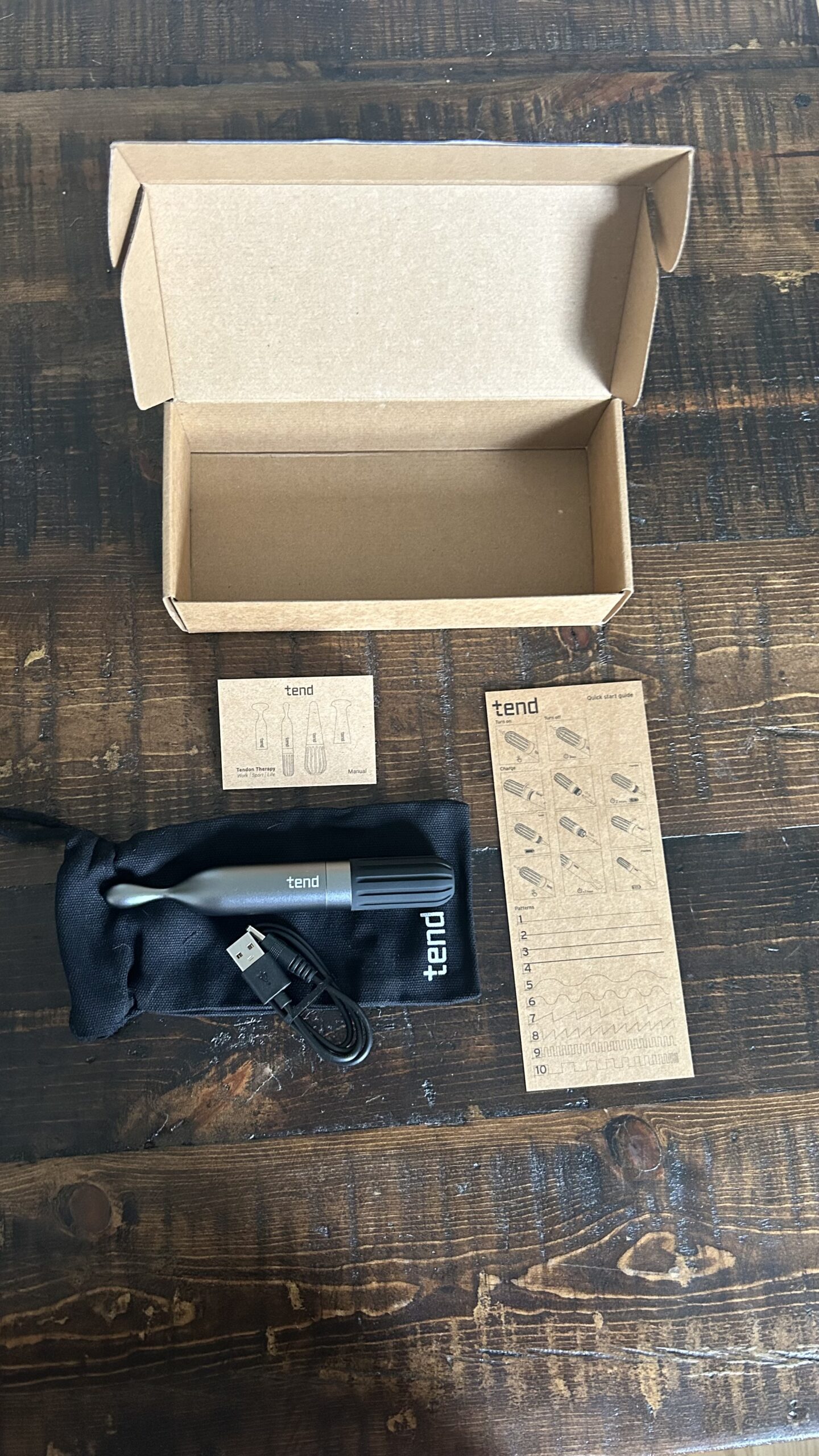 A Tend electric toothbrush kit on a wooden table, including the toothbrush, USB charging cable, cloth pouch, user manual, instructions, and an open cardboard box.