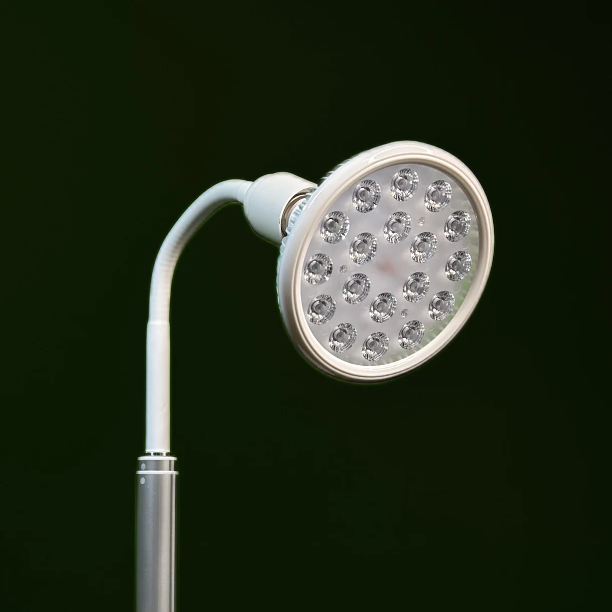 A close-up of a modern LED examination lamp with multiple circular light bulbs, its sleek design reminiscent of cutting-edge massage guns, set against a dark green background.