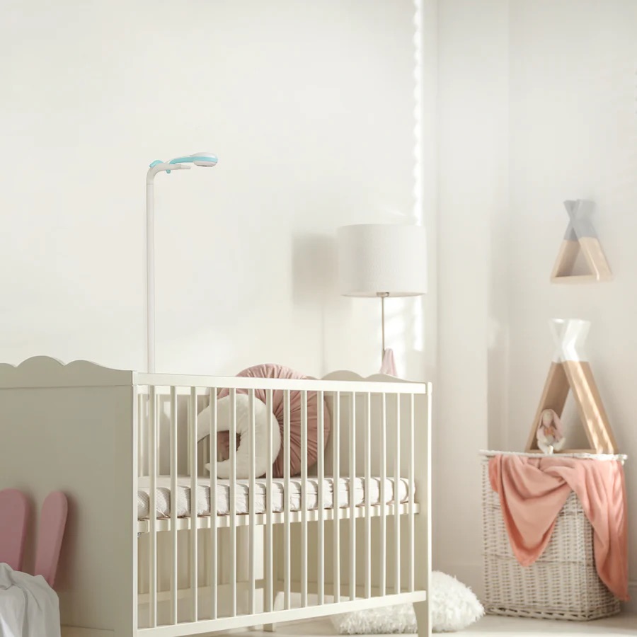 A white crib with a small lamp stands in a softly lit nursery, decorated with a basket, plush toys, and a lamp on a table—creating a calm space perfect for unwinding after using massage guns.